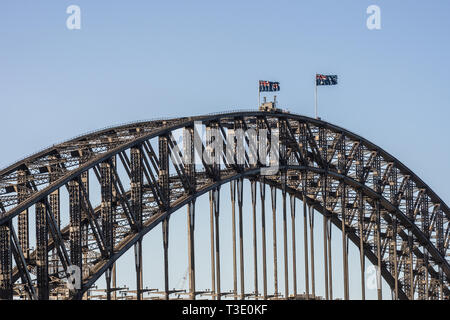 Sydney, Australia - February 12, 2019: Closeup of Harbour bridge span during sunset. Black metal, Flags and light blue sky. Stock Photo