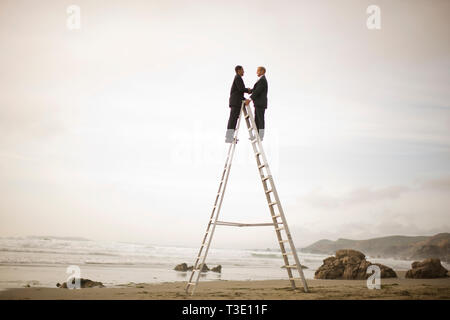 Businessmen shaking hands on ladder at beach Stock Photo
