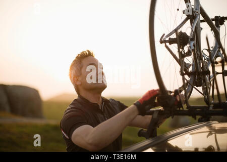Male cyclist lifting his bike off the top of his car Stock Photo