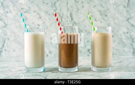 Vanilla, chocolate and cinnamon flavoured almond milk in glasses on white marble countertop. Stock Photo