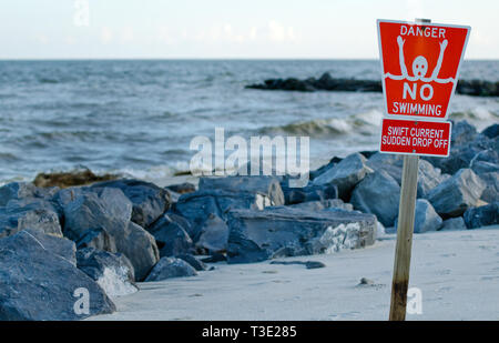 A 'No Swimming' sign warns swimmers of swift currents and the danger of rip currents and a strong undertow around jetties in Dauphin Island, Alabama. Stock Photo
