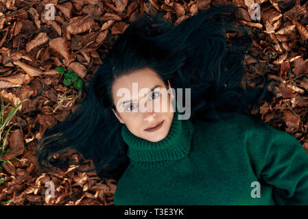 Outdoor portrait of a black haired woman lying on the ground in leafs