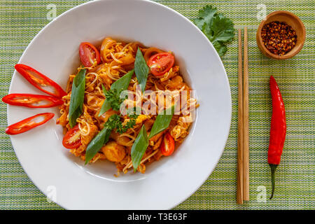 Thai traditional noodle dish Pad Thai served on white ceramic plate. Wooden chopsticks and dry chili on the side. Top view. Stock Photo