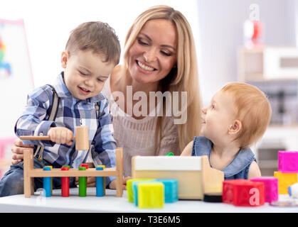 Kindergarten teacher and children playing together in nursery or daycare centre Stock Photo