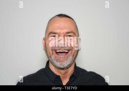Joyful bearded middle-aged man laughing at the camera enjoying a good joke over a grey studio background Stock Photo