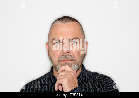 Middle-aged man deep in thought with hand to chin staring upwards with a contemplative expression in a close up head and shoulders portrait Stock Photo