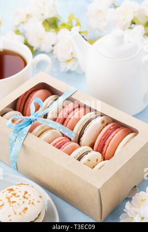 Gift box with french macarons and tea for dessert. Flowers in the background. Stock Photo