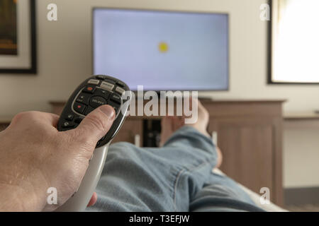 Hand Holding remote Control for television while relaxing with feet propped up Stock Photo
