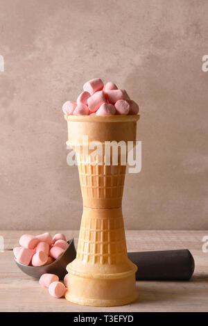 Stacked ice cream cones filled with pink marshmallows and a scoop in the background. Stock Photo