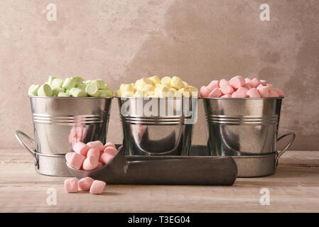 Three small pails filled with colored marshmallows with an ice cream scoop and pink marshmallows in the foreground. Stock Photo