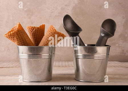 Closeup of three ice cream cones in a small metal bucket next to a pail with two scoops. Stock Photo