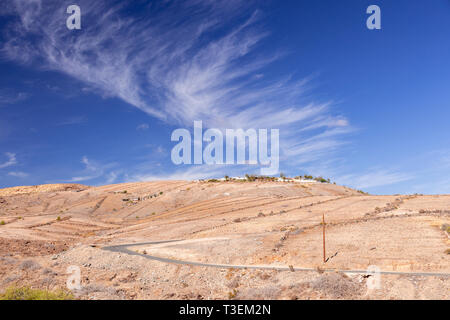 Road through dry landscape at Meloneras, Gran Canaria, Canary Islands with cirrus clouds overhead Stock Photo