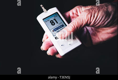 Small portable digital blood glucose meter use by a senior woman diabetic to self monitor and medicate the disease Data at normal blood sugar level Stock Photo