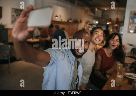 Smiling friends taking selfies together in a bar Stock Photo