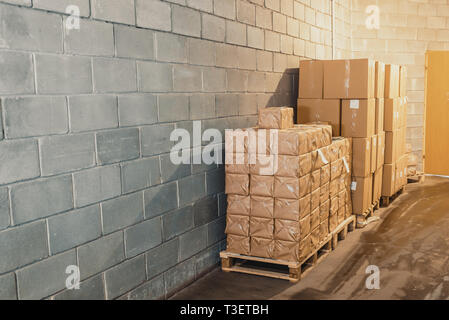 Cardboard boxes on pallets in warehouse near the concrete wall Stock Photo