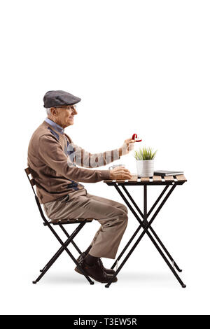 Full length profile shot of a senior man sitting at a cafe and holding a ring in a box isolated on white background Stock Photo