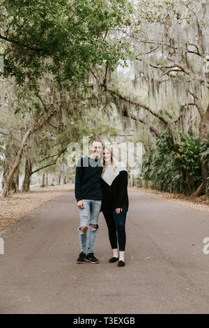 Cute Young Happy Loving Couple Walking Down an Old Abandoned Road with Mossy Oak Trees Overhanging Stock Photo