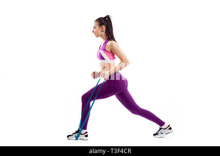 Sporty woman does  exercises on legs, makes lunges  with sport fitness rubber bands  on white background. Photo of muscular woman in sportswear on whi Stock Photo