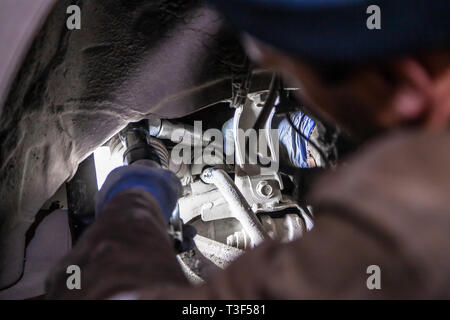 Close up Professional car mechanic makes repairs to the undercarriage of a supported car in auto repair service. Autoworker changes sleeves in garage  Stock Photo