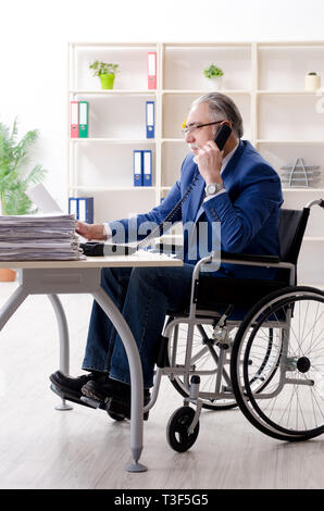 Aged employee in wheelchair working in the office Stock Photo
