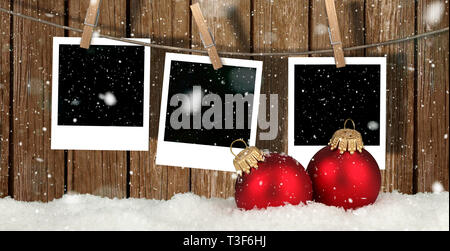 blank instant photos hanging on the clothesline in front of wooden background with snow and christmas balls - christmas background Stock Photo
