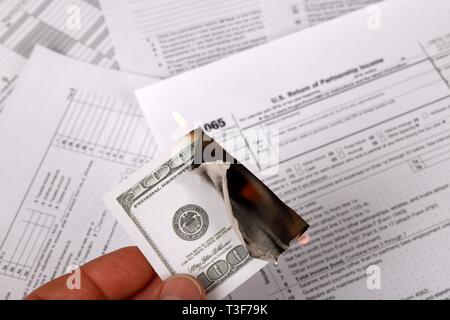 1065 tax form and a burning hundred dollar bill on a Table. US Return for parentship income Stock Photo