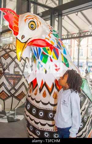 Giant Easter paper-mache oversize chicken on display in the city centre. TADIWA CHAPARADZA (MR) 10 years old is intrigued by the Papier-Mache big cockerel sculpture.  Easter festive animal figures on display standing at two-metres tall, the attractions are to placed outside Preston Market. Keith Ogden, a local artist, is the man behind the hand painted attraction. The eggs are themed around the the city's industrial heritage and Lancashire landscapes. Preston Markets are to exhibit the Giant Easter Eggs for selfie competition over the Easter holidays. Stock Photo