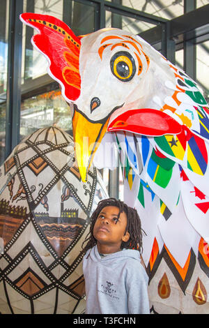 Giant Easter paper-mache oversize chicken on display in the city centre. TADIWA CHAPARADZA (MR) 10 years old is intrigued by the Papier-Mache big cockerel sculpture.  Easter festive animal figures on display standing at two-metres tall, the attractions are to placed outside Preston Market. Keith Ogden, a local artist, is the man behind the hand painted attraction. The eggs are themed around the the city's industrial heritage and Lancashire landscapes. Preston Markets are to exhibit the Giant Easter Eggs for selfie competition over the Easter holidays. Stock Photo