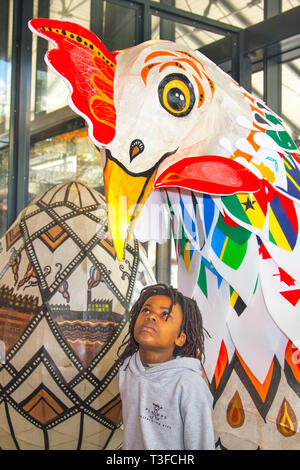 Giant Easter paper-mache oversize chicken on display in the city centre. TADIWA CHAPARADZA (MR) 10 years old is intrigued by the Papier-Mache big cockerel sculpture.  Easter festive animal figures on display standing at two-metres tall, the attractions are to placed outside Preston Market. Keith Ogden, a local artist, is the man behind the hand painted attraction. The eggs are themed around the the city's industrial heritage and Lancashire landscapes. Preston Markets are to exhibit the Giant Easter Eggs for selfie competition over the Easter holidays. Stock Photo