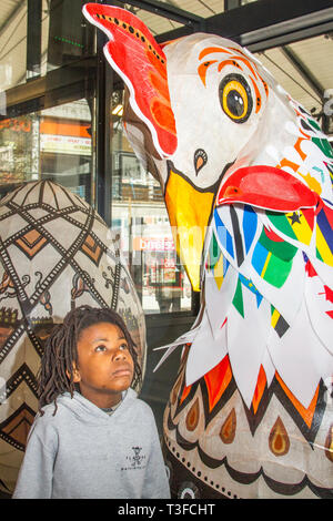 Giant Easter paper-mache oversize chicken on display in the city centre. TADIWA CHAPARADZA (MR) 10 years old is intrigued by the Papier-Mache big cockerel sculpture.  Easter festive animal figures on display standing at two-metres tall, the attractions are to placed outside Preston Market. Keith Ogden, a local artist, is the man behind the hand painted attraction. The eggs are themed around the the city's industrial heritage and Lancashire landscapes. Preston Markets are to exhibit the Giant Easter Eggs for selfie competition over the Easter holidays. Stock Photo