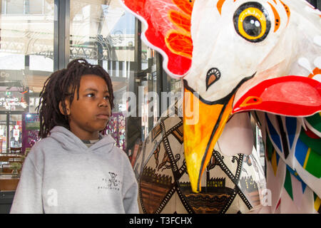 Giant Easter paper-mache oversize chicken on display in the city centre. TADIWA CHAPARADZA (MR) 10 years old is intrigued by the Papier-Mache big cockerel sculpture.  Easter festive animal figures on display standing at two-metres tall, the attractions are to placed outside Preston Market. Keith Ogden, a local artist, is the man behind the hand painted attraction. The eggs are themed around the the city's industrial heritage and Lancashire landscapes. Preston Markets are to exhibit the Giant Easter Eggs for selfie competition over the Easter holidays. Stock Photo