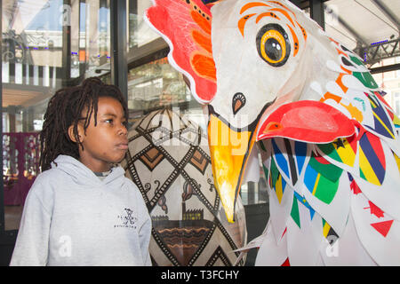 Giant Easter paper-mache oversize chicken on display in the city centre. TADIWA CHAPARADZA (MR) 10 years old is intrigued by the Papier-Mache big cockerel sculpture.  Easter festive animal figures on display standing at two-metres tall, the attractions are to placed outside Preston Market. Keith Ogden, a local artist, is the man behind the hand painted attraction. The eggs are themed around the the city's industrial heritage and Lancashire landscapes. Preston Markets are to exhibit the Giant Easter Eggs for selfie competition over the Easter holidays. Stock Photo