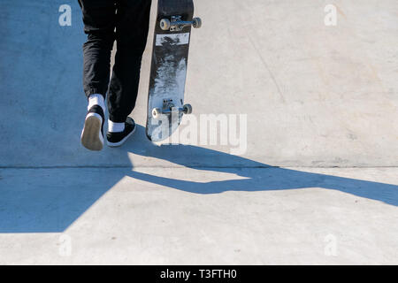 Young skateboard athlete walking up the ramp while holding a skateboard. Practice freestyle, urban extreme sport activity for youth, staying out of tr Stock Photo