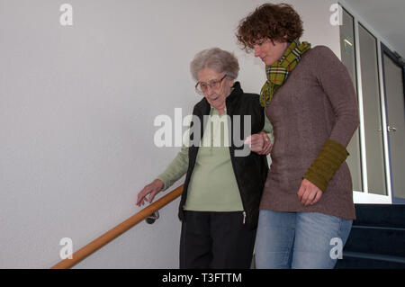 Caregiver helping senior woman walking down the stairs Stock Photo