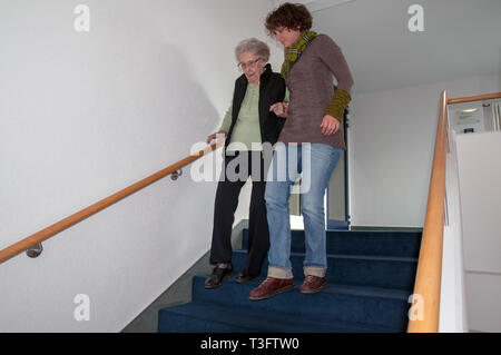 Caregiver helping senior woman walking down the stairs Stock Photo