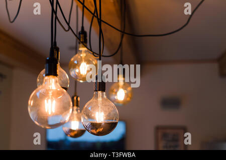 Close up view of vintage decorative light lamp bulb glowing on the ceiling indoors. Transparent lamps glowing with warm light Stock Photo