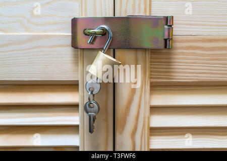 Metal lock with keys hanging on modern wooden cabinet with strips in classic rustic style. Locker wardrobe closet with shutter plank doors Stock Photo