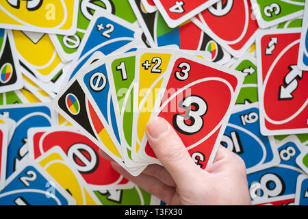 6 April 2019, Wuhan China : Man hand holding Uno game cards and cards scattered all over in background Stock Photo