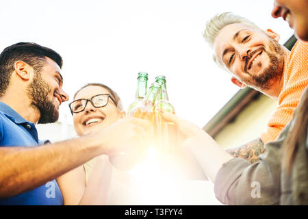 Happy friends toasting beers at sunset outdoor - Young people having fun cheering and drinking alcohol at rooftop - Friendship concept Stock Photo