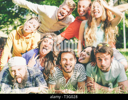 Group of friends having fun together lying on grass while making a self portrait with silly faces - Young happy people taking photo of group Stock Photo