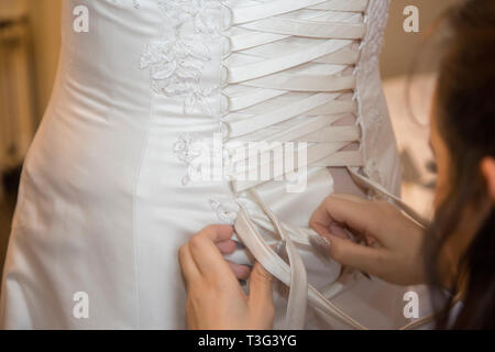 Wedding dress being done up by a bridesmaid on the Brides wedding day, the dress is laced up the back Stock Photo