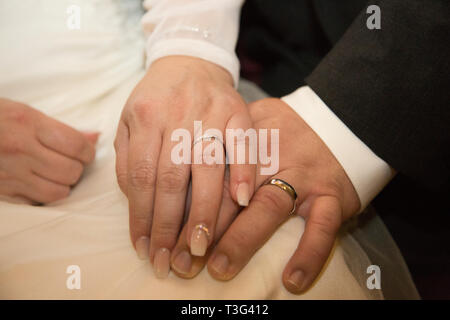 bride and groom holding hands showing their wedding rings, resting on the brides lap Stock Photo
