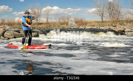 Senior paddler is paddling inflatable stand up paddleboard on a turbulent river below a grade control structure - South Platte River in northern Color Stock Photo