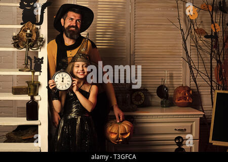 Wizard and little witch in hats hold clock and pumpkin Stock Photo