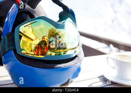 Reflections of woman and children and beautiful mountains on a ski goggles, glass of wine, coffee and cake Stock Photo