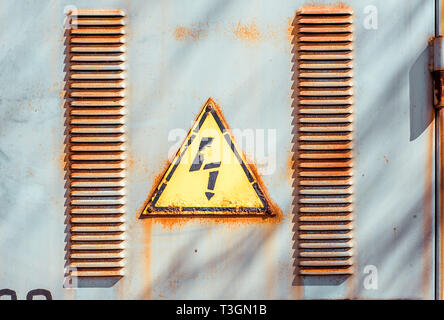 Yellow sign danger electricity between two rows of perforated air vents on steel door in switchboard. Texture with paint stains and rusty. Stock Photo