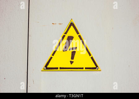 Yellow sign danger electricity on steel door in switchboard. Texture with paint stains and rusty. Stock Photo