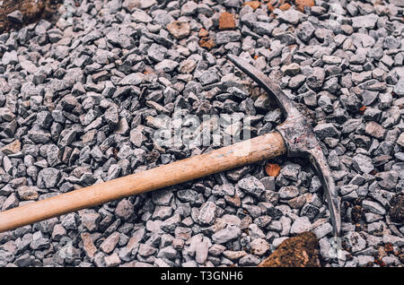 Metal pickaxe on a wooden handle on a pile of small rubble. Dirty hard work. Stock Photo