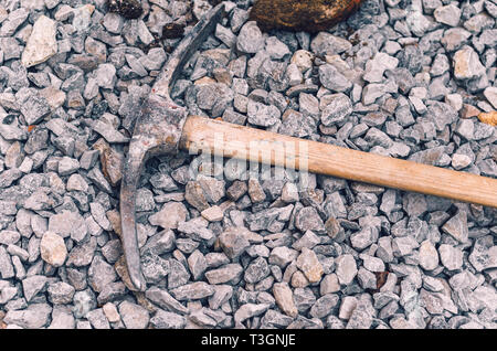 Metal pickaxe on a wooden handle on a pile of small rubble. Dirty hard work. Stock Photo
