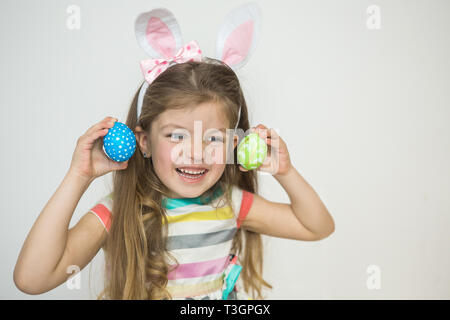 Cute little girl wearing bunny ears holding painted Easter eggs and smiling. Stock Photo